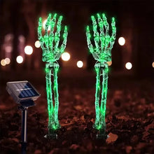 Glowing skeleton hand solar lights staked in a yard at night