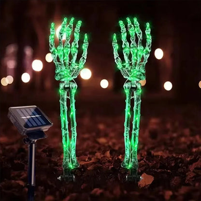 Glowing skeleton hand solar lights staked in a yard at night