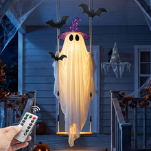 Large canvas swing ghost decoration with two witch hats and lit string lights hanging outdoors
