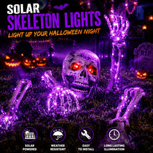 Five solar skeleton arm and skull head ground stake lights glowing in a yard at night