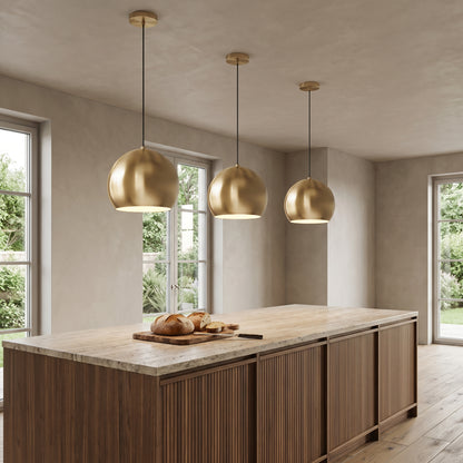 Three Vesper brass globe pendant lights in gold above a walnut kitchen island