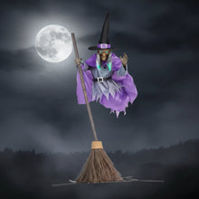 Witch silhouette decoration hanging from a porch beam in a Halloween yard display