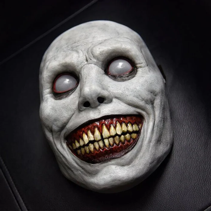 Creepy smiling costume mask in soft latex, with a wide grin, yellow teeth and blank white eyes